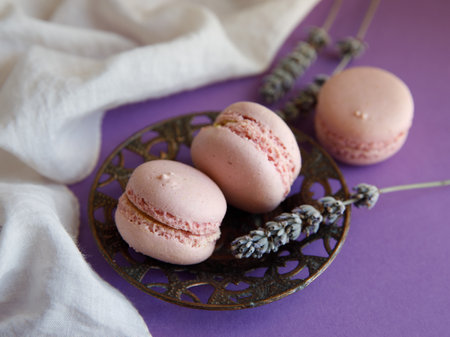 three pink pastel macaroons close-up on vintage metal plat on bright purple background with lavender flower and white cloth, Delicious strawberry raspberry cookies. Top view flat layの写真素材