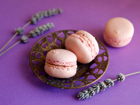 three pink pastel macaroons close-up on vintage metal plat on bright purple background with lavender flower, Delicious strawberry raspberry cookies. Top view flat layの写真素材