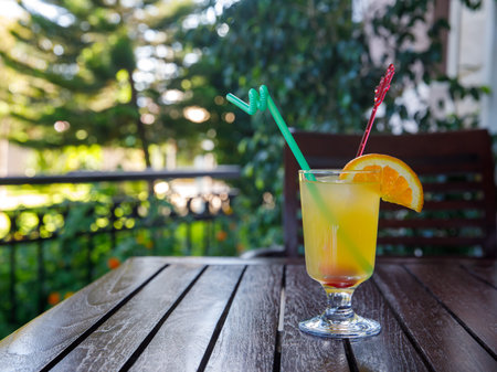Glass of non alcoholic yellow juice Conga cocktail on table outdoors at tropical resort with palm tree. Horizontal. Healthy fresh cold drink. Vegetarian cocktail party. copy spaceの写真素材