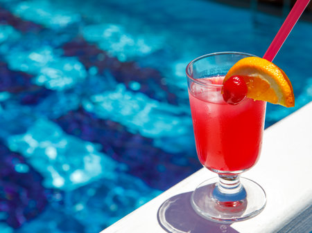 Glass of non alcoholic Pink panther cocktail on pool nosing at tropical resort. Horizontal, cocktail on right side. Healthy fresh cold drink. Pool cocktail party. copy spaceの写真素材