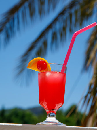 Glass of non alcoholic Pink panther cocktail on table or balcony at tropical resort with palm tree. vertical. Healthy fresh cold drink. Vegetarian cocktail party. copy spaceの写真素材