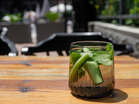Cucumber and mint leaves infused water, cocktail, lemonade in glass in cafe. Summer iced cold drink with cucumber, ice and mint on wooden table outside background, copy space, side viewの写真素材