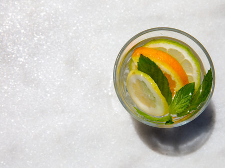 Citrus and mint leaves infused water, cocktail, lemonade in glass. Summer iced cold drink with lemon, lime, orange, ice and mint on white marble background, copy space, top viewの写真素材