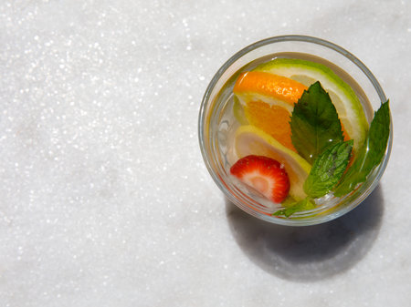 Citrus and mint leaves infused water, cocktail, lemonade in glass. Summer iced cold drink with lemon, lime, orange, strawberry, ice and mint on white marble background, copy space, top viewの写真素材