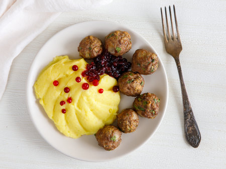 Swedish Kottbullar meatball with mashed boiled potatoes and cowberry sauce on white plate on white background. top view.の写真素材