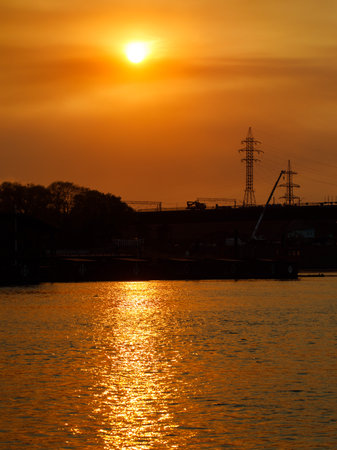 bright colorful orange sunset on the city's waterfront with reflection of sun in the water and silhouette of power line support. vertical. Novosibirsk, Russiaの写真素材