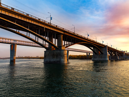 Two bridges: arched October road bridge and metro subway bridge over the Ob River in the big city Novosibirsk at sunset,の写真素材