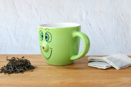 A green smiling cup choose between tea leaves and tea bags. Concept of natural food choice and environmental protectionの写真素材