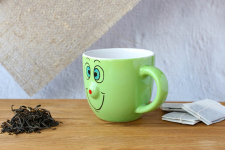 A green smiling cup choose between tea leaves and tea bags. Concept of natural food choice and environmental protectionの写真素材