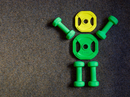 Green heavy dumbbells and yellow barbell metal weight disc in shape of human body on black background. Fitness and training composition with copy space. Top view from above, flat layの写真素材