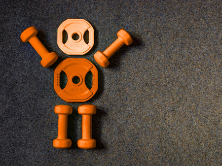 Orange heavy dumbbells and yellow barbell metal weight disc in shape of human body on black background. Autumn fitness and Halloween training composition with copy space. Top view from above, flat layの写真素材