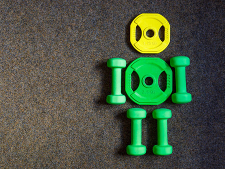 Green heavy dumbbells and yellow barbell metal weight disc in shape of human body on black background. Fitness and training composition with copy space. Top view from above, flat layの写真素材