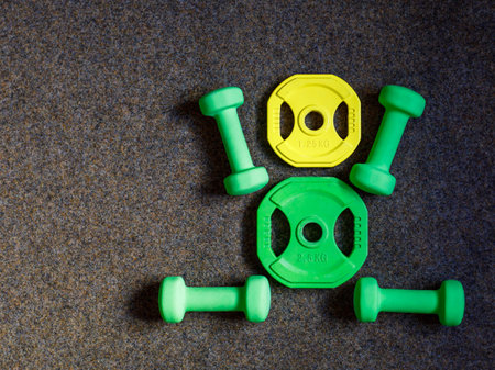 Green heavy dumbbells and yellow barbell metal weight disc in shape of human body on black background. Fitness and training composition with copy space. Top view from above, flat layの写真素材