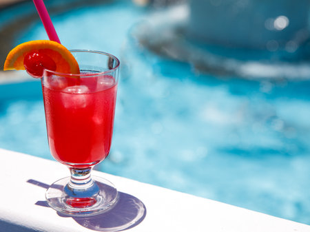 Glass of non alcoholic Pink panther cocktail on pool nosing at tropical resort. Horizontal, cocktail on left side. Healthy fresh cold drink. Pool cocktail party vegetarian. copy spaceの写真素材
