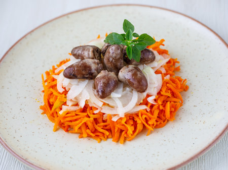 Chicken hearts, carrot and onion fresh tasty salad on white plate on wooden table. Top view flat layの写真素材