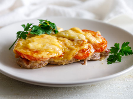 Baked Pork Steak with Tomato slice grated with cheese on white plate close up.の写真素材