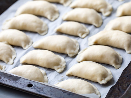 Homemade vareniki or dumplings, filled with cottage cheese or mashed potato on baking sheet. Cooking raw dumplings with potatoes. Top view, rural style. Ukrainian and Russian national dish.の写真素材