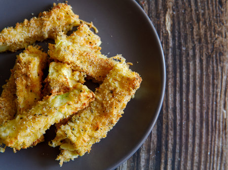 crunchy zucchini sticks breaded with breadcrumbs, parmesan cheese, spices on a black plate on a wooden table, top view from above, flat lay, close up, copy spaceの写真素材