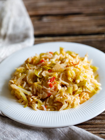 Traditional homemade Mediterranean Crete cuisine rice with vegetables cabbage, onion and tomato on white plate with fork and napkin on old wooden table. Vegetarian healthy lunch, dinner idea Side viewの写真素材