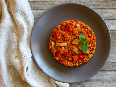 Healthy vegetarian homemade lentil stew with vegetables on a plate with basil leaf on rustic wooden table with napkin. Vegan diet. Top view, flat lay.の写真素材