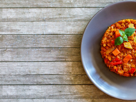 Healthy vegetarian homemade lentil stew with vegetables on a plate with basil leaf on rustic wooden table. Vegan diet. Top view, flat lay, copy space.の写真素材