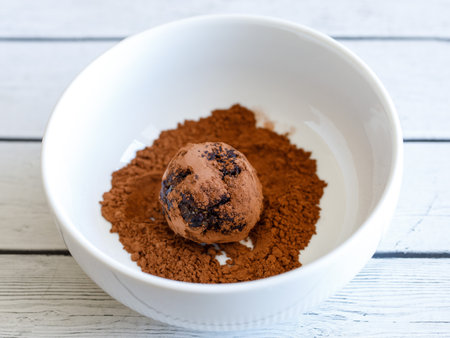 Healthy organic homemade delicious energy ball: chocolate balls cakes made from raisin, prune, dates, walnut, figs on white background, covering in bowl with cocoa carob powder. close up top viewの写真素材