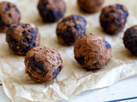 Healthy organic homemade delicious energy balls: chocolate balls cakes made from raisin, prune, dates, walnut, figs on baking paper against white background, covered with cocoa carob powder. close upの写真素材