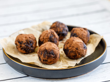 Healthy organic homemade delicious energy balls: chocolate balls cakes made from raisin, prune, dates, walnut, figs in black plate against white background, covered with cocoa carob powder. close upの写真素材