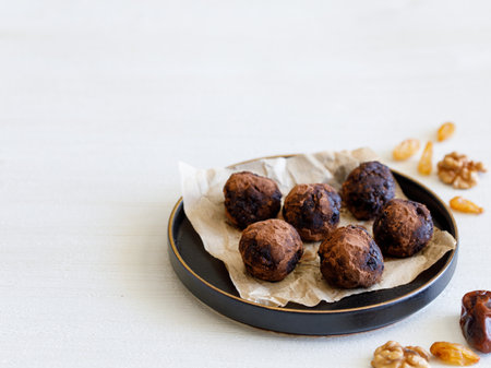 Healthy homemade delicious energy balls: chocolate ball cakes made from raisin, prune, dates, walnut, figs in black plate against white background, covered with cocoa carob powder. close up copy spaceの写真素材