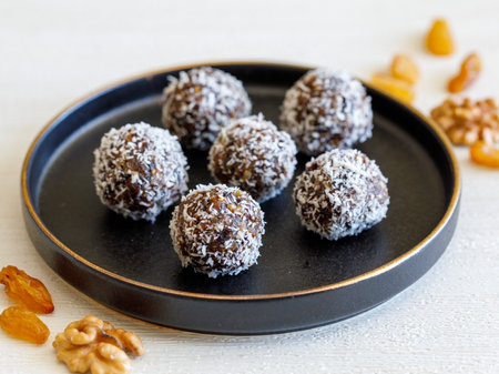 Healthy organic homemade delicious energy balls: dry fruit ball cakes made from raisin, prune, dates, walnut, figs in black plate against white background, covered with coconut flakes. close upの写真素材