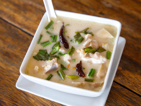 Tom kha kai in ceramic bowl on wooden table. Tom Kha Gai is Thai traditional spicy, sour and hot soup with coconut milk. Thai and Lao cuisines.の写真素材