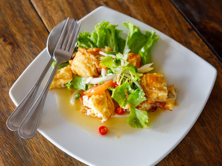 Yam khai dao fried egg spicy sour salad with vegetables and herbs is a Thai dish close up in the plate on wooden table. Top view from aboveの写真素材