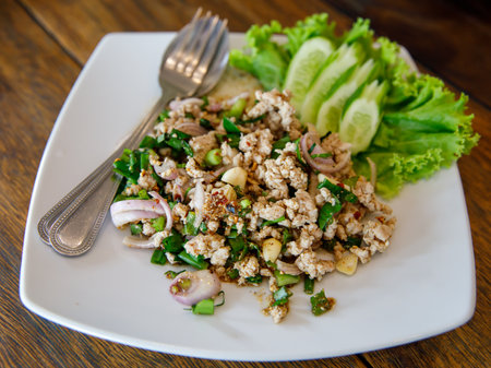 Thai food, spicy minced pork salad Larb Moo on white dish with spoon and fork on wooden background, close upの写真素材