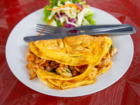 Stuffed Thai Omelette with meat and vegetables on white plate, fork and spoonの写真素材