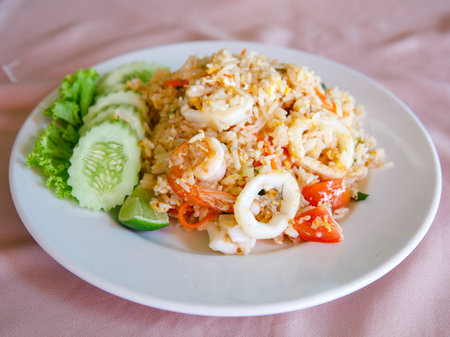 Delicious Fried rice with seafood, egg, garlic, cucumber, lemon. Thai food called Khao pad thale. Shrimp, squid, octopus, crab Fried Rice on white ceramic plate. selective focusの写真素材