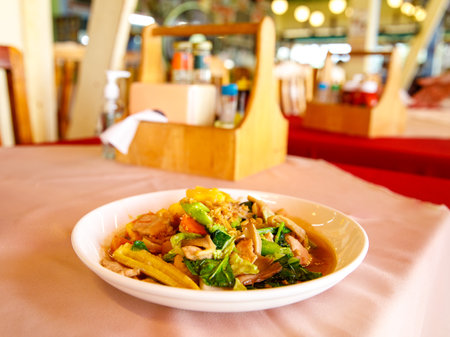 Stir-fried mixed vegetables with pork and oyster sauce in white plate on table in thai cafe. Thailand healthy and delicious food, blureed background, selective focusの写真素材