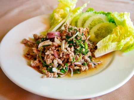 Thai food, spicy minced pork salad Larb Moo on white dish with spoon and fork on wooden background, close upの写真素材