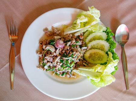 Thai food, spicy minced pork salad Larb Moo on white dish with spoon and fork on wooden background, top viewの写真素材