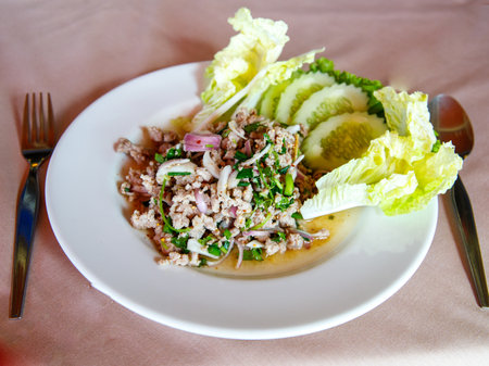 Thai food, spicy minced pork salad Larb Moo on white dish with spoon and fork on wooden background, close upの写真素材
