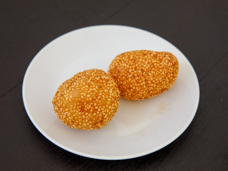 Khanom Kai Hong with sesame or Swan Eggs Dessert, native Thailand fried dessert balls like doughnuts on white plate on black wooden backgroundの写真素材