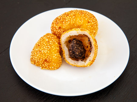 Khanom Kai Hong with sesame or Swan Eggs Dessert, native Thailand fried dessert balls like doughnuts with black bean paste on white plate on black wooden backgroundの写真素材