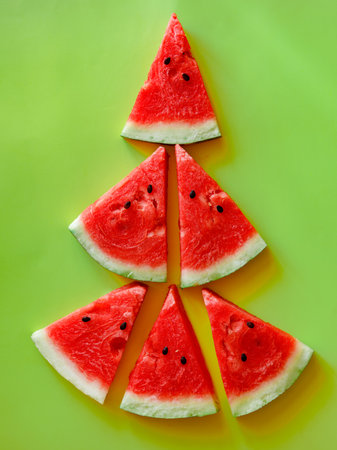 New Year's food. Edible Christmas tree made of watermelon slices on a green background, top view. Christmas decor on the table. Festive still life. Creative ideas for Christmas breakfast. verticalの写真素材
