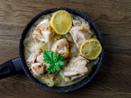 Greek stewed chicken with lemons, onions and scented leaved pelargonium leaves close-up on a iron pan on a table. horizontal, top view flat lay.の写真素材