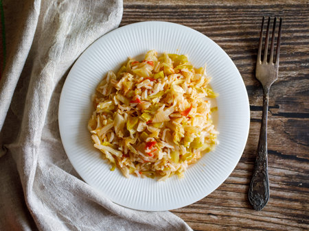 Traditional homemade Mediterranean Crete cuisine rice with vegetables cabbage, onion and tomato on white plate with fork and napkin on old wooden table. Vegetarian healthy lunch, dinner idea. top viewの写真素材