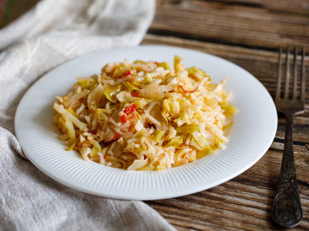 Traditional homemade Mediterranean Crete cuisine rice with vegetables cabbage, onion and tomato on white plate with fork and napkin on old wooden table. Vegetarian healthy lunch, dinner idea Side viewの写真素材