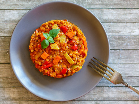 Healthy vegetarian homemade lentil stew with vegetables on a plate with basil leaf on rustic wooden table with fork. Vegan diet. Top view, flat lay.の写真素材