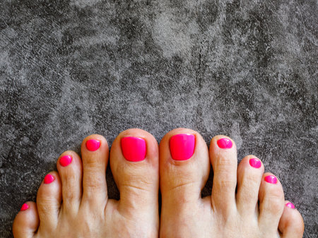 Beautiful woman's neon pink nails with beautiful pedicure. Female feet with bright pedicure on black marble background. Spring and summer concept. Top view, copy space, horizontal, close up.の写真素材
