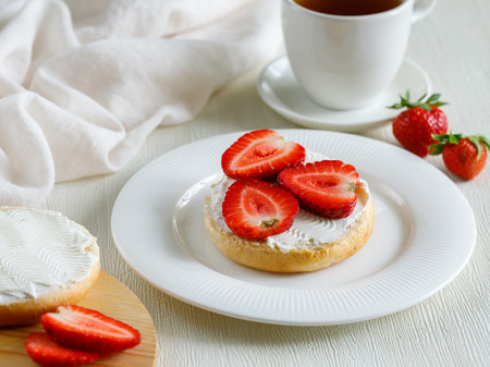 Tasty bruschetta with cream cheese and slices of ripe strawberries on white plate with cup of tea on white background. side view, close up.の写真素材
