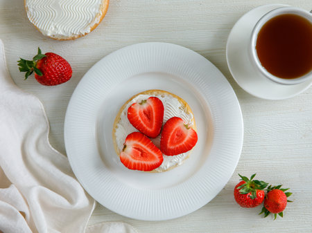 Top view of tasty bruschetta with cream cheese and ripe strawberries on white plate with cup of tea on white background.の写真素材