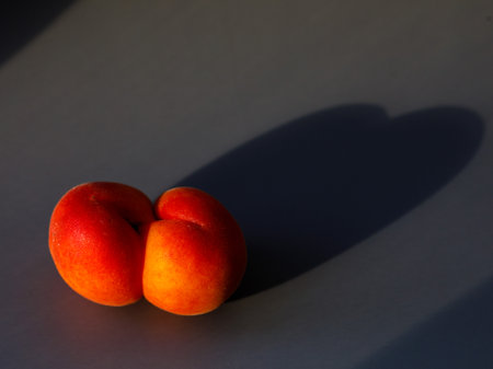 One ugly apricot with hard shadow in heart shape on dark gray background in minimal style. Creative fresh summer fruit layout. Vegan food fun concept. trend wallpaper website blog design pop artの写真素材
